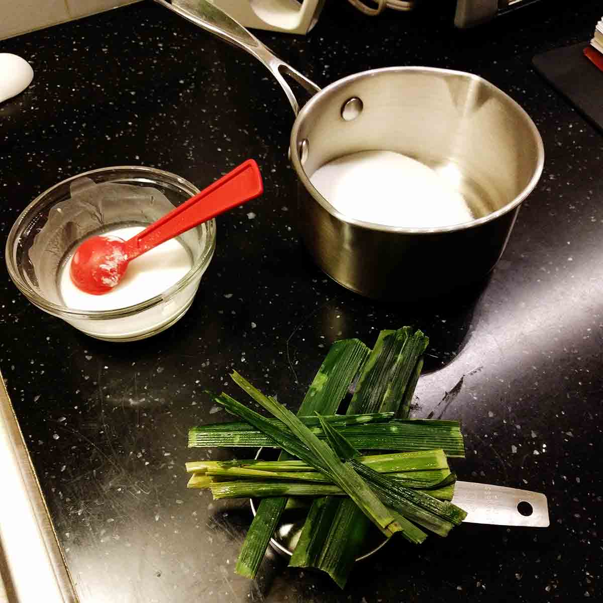 Kaya recipe, showing the corn starch mixture in a bowl, the sugar in a saucepan, and the pandan leaves.