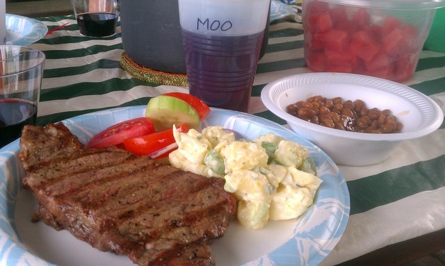 Steak, tomato cucumber salad, potato salad, baked beans, watermelon.