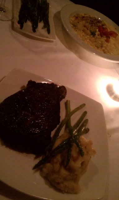 16oz. strip steak, mashed spuds, asparagus; mac-n-cheese in the background.