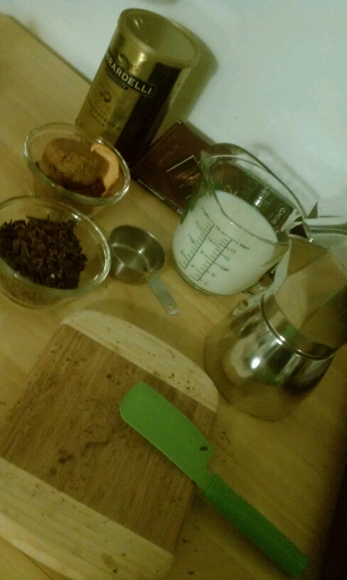 Small bowls with chopped chocolate, orange rind, cocoa powder, and brown sugar; these sit next to a measuring cup of milk, a Moka pot base, a cutting board, a tub of Ghirardelli cocoa powder, and a tiny green cleaver.