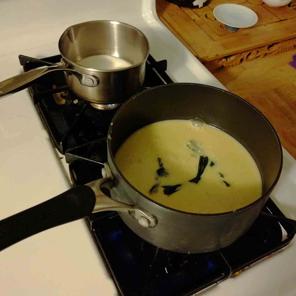 Kaya recipe, showing the egg mixture and pandan leaf knots in one saucepan, sugar in another saucepan.