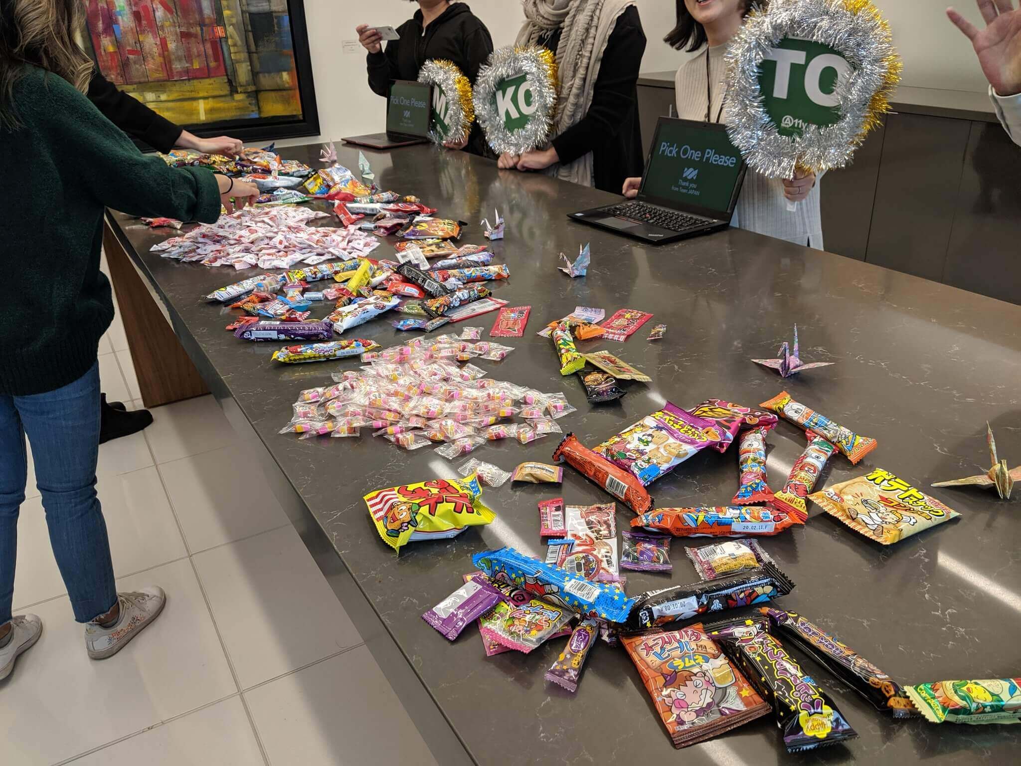 A long table covered with Japanese candies and a team from Japan standing behind it.