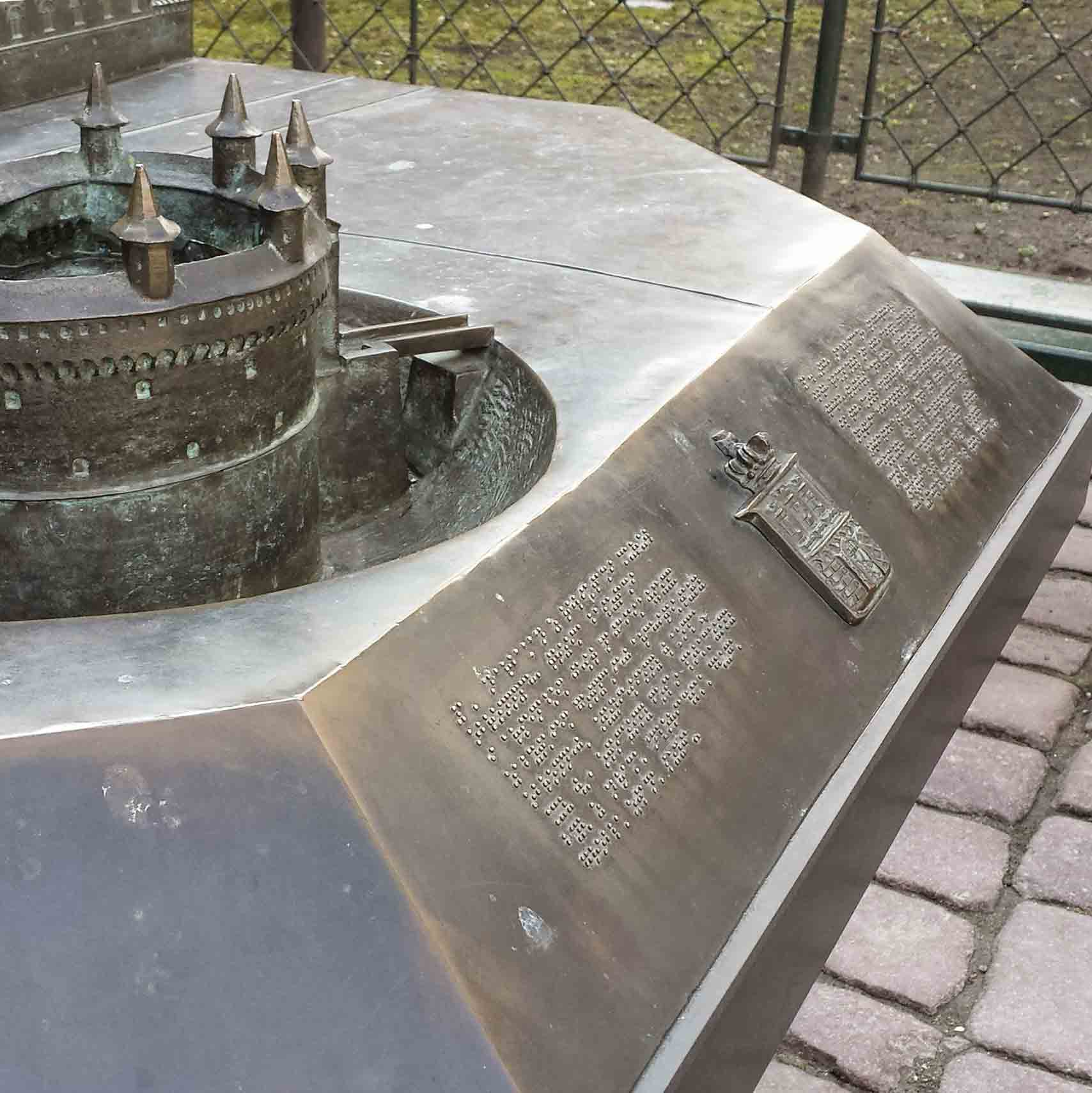 Outdoor metal tactile map / sculpture of a fortress with a Braille explainer set in front of it.