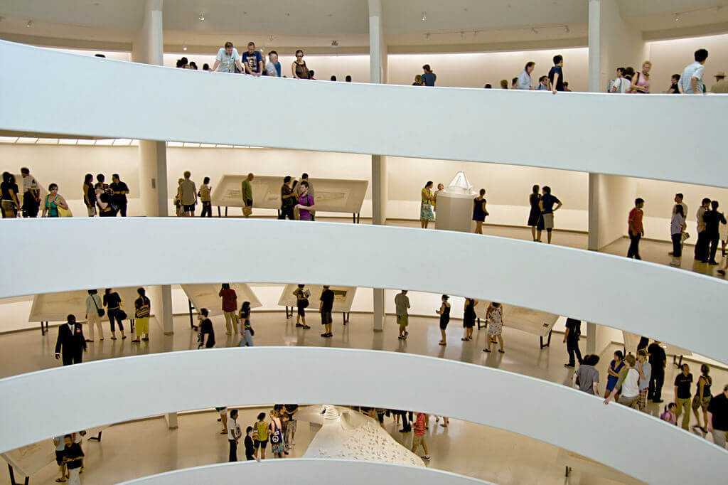 Looking across the atrium with four levels of the gallery space / ramp visible. The ramp contains exhibits as well as crowds of people moving among them, with some people leaning over the edge of the ramp wall.