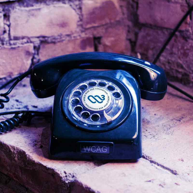 Rotary phone with the 2025 W3C logo in the center, ‘WCAG’ as a label at the base, and sitting in a deep brick window.