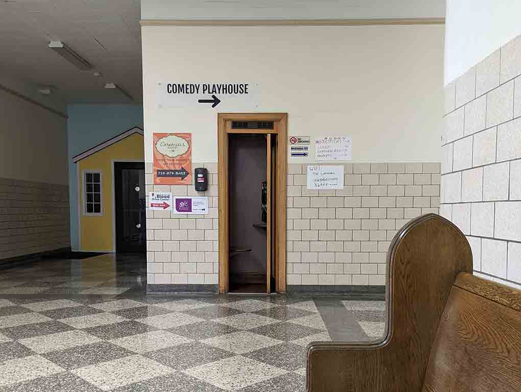 A step-in phonebooth built flush into a wall in an old school hallway with institutional floors and walls.