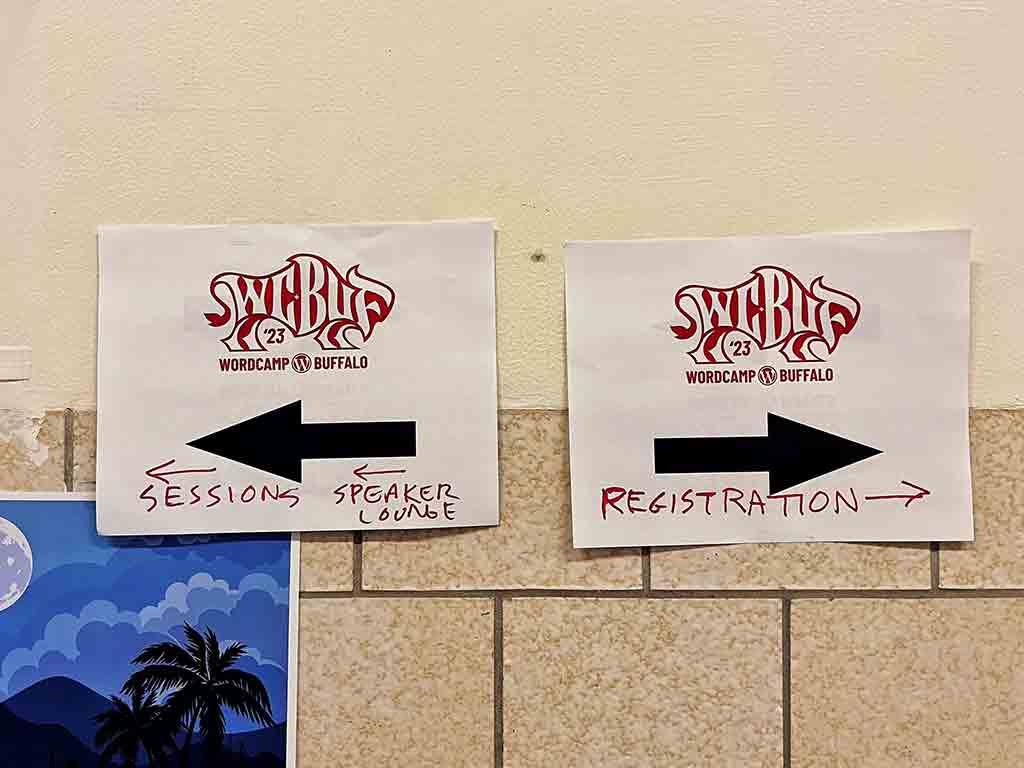Two WordCamo Buffalo signs with arrow pointing in opposite directions. One sign points to sessions & speaker lounge. The other sign points to registration.