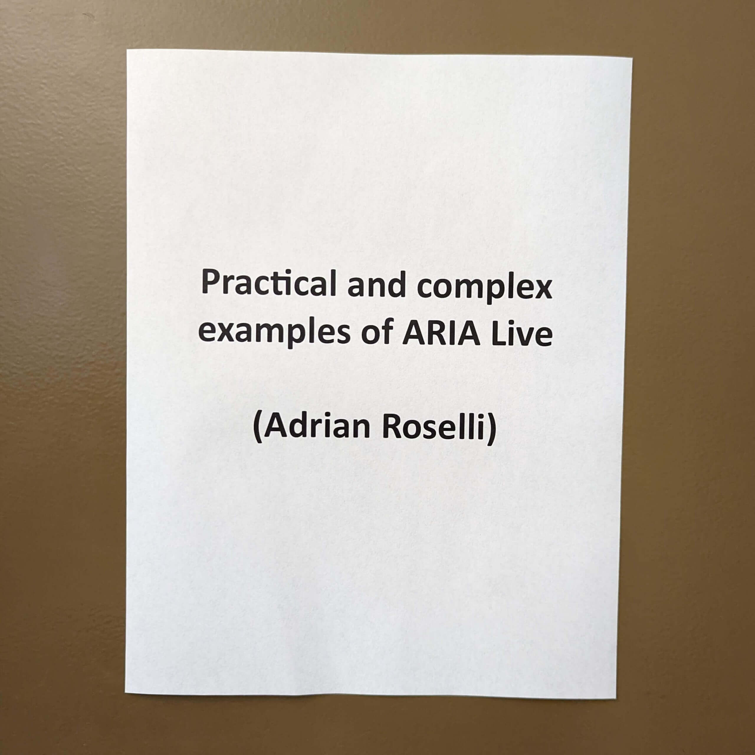 On a brown metal door is taped a white sheet of paper with the text: Practical and complex examples of ARIA live (Adrian Roselli)