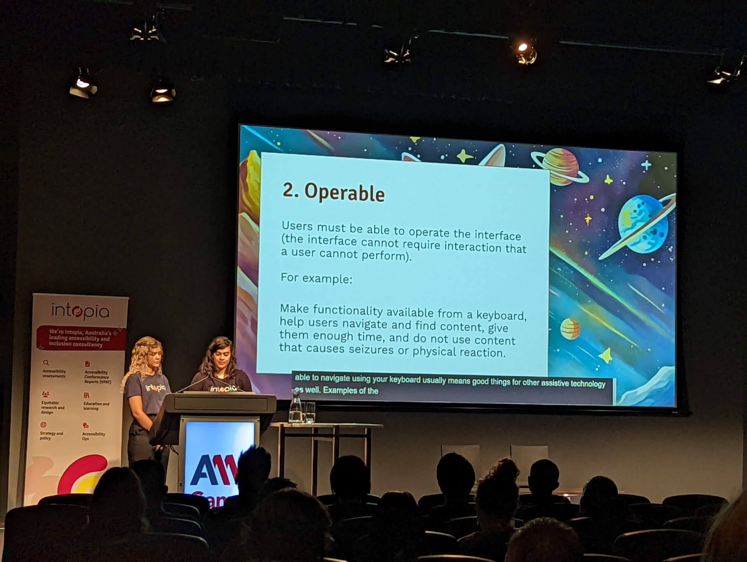 Two women on stage in front of a slide explaining the Operable principle from WCAG.