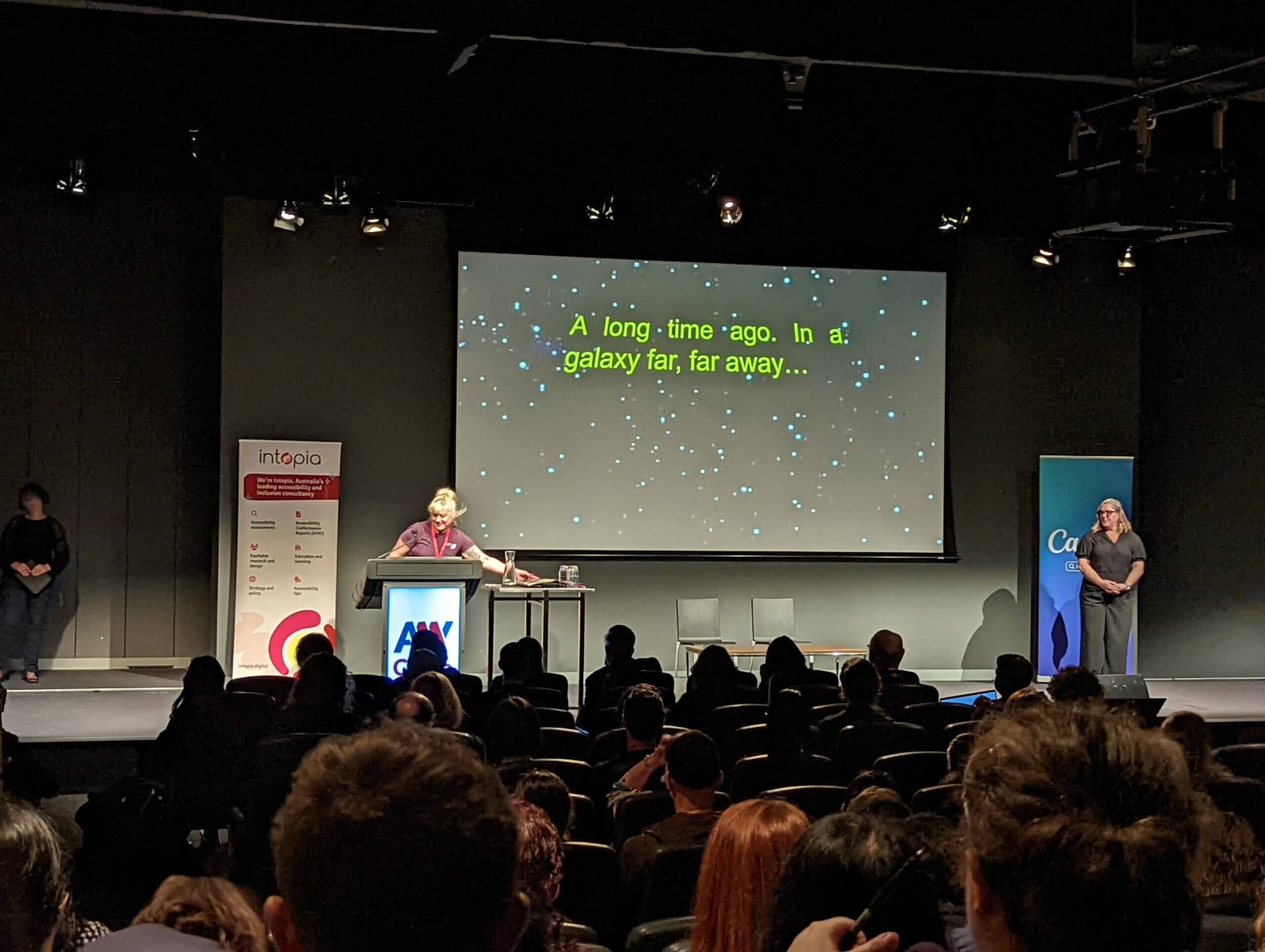 A woman with light hair is stepping onto the stage while yellow text scrolls up a starfield, reading ”A long time ago, in a galaxy far, far away.”