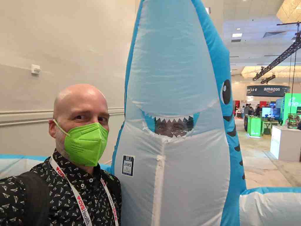 Selfie of me in a bright green N95 mask with a man in an inflatable shark costume over my shoulder.