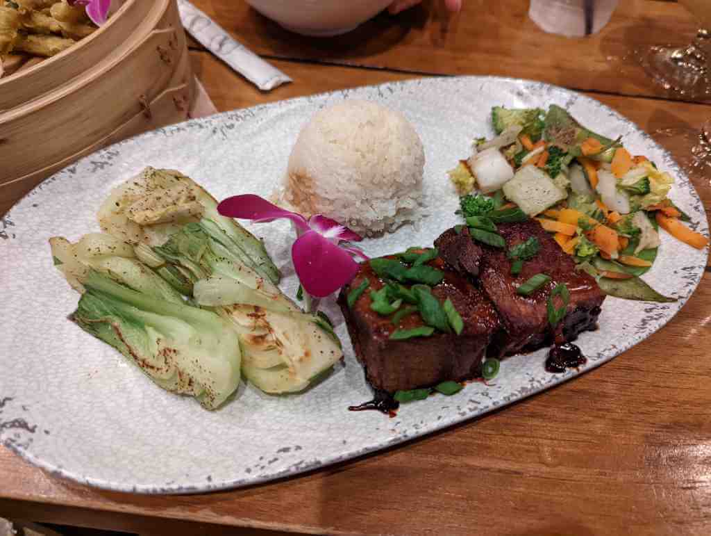 An oblong plate with four bok choy halves dusted with pepper, a round scoop of plain white rice, two squares of beef in sauce, and a steamed vegetable medley with only black pepper.