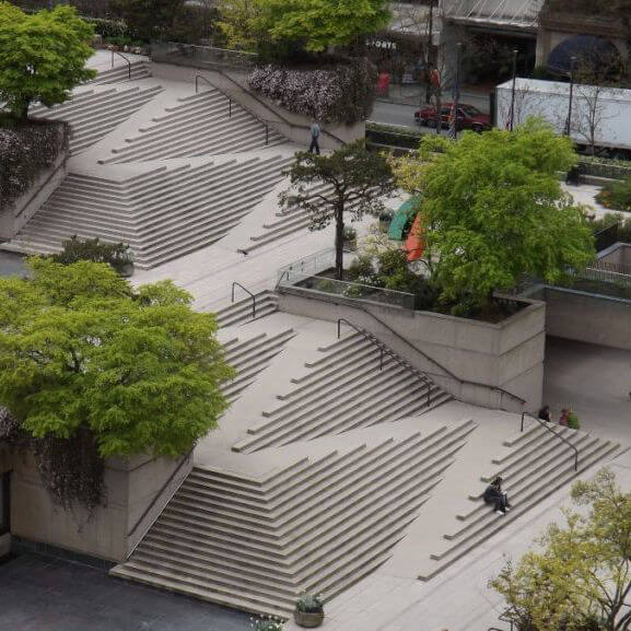 Two wide concrete staircases with a steep ramp slashing through them in a zig zag, each turn at a wall or open to the stairs below it.