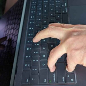 A Mac keyboard with a hand contorting its fingers to as it presses Control, Option, Caps Lock, and a fourth finger is reaching for the J.